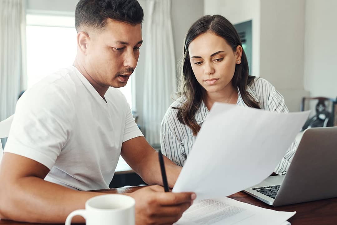 A married couple reviewing their family's financial documents and other paperwork for a loan refinancing.